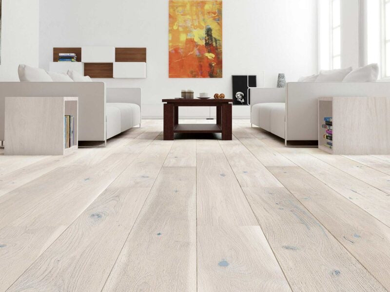 Modern living room with light wood flooring, white walls, and a colorful abstract painting.